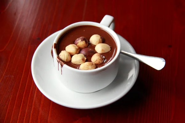 Chocolate caliente con nueces en una taza blanca sobre una mesa marrón — Foto de Stock