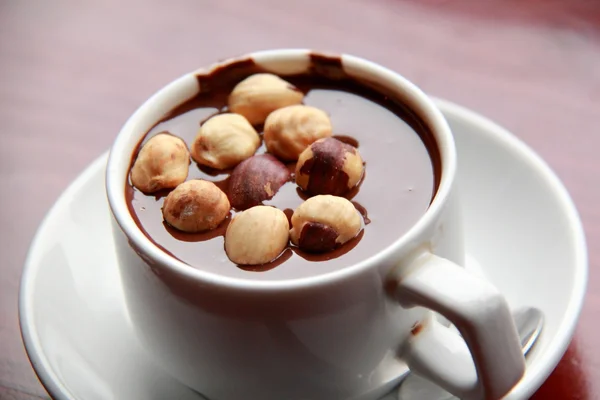 Chocolate caliente con nueces en una taza blanca sobre una mesa marrón — Foto de Stock