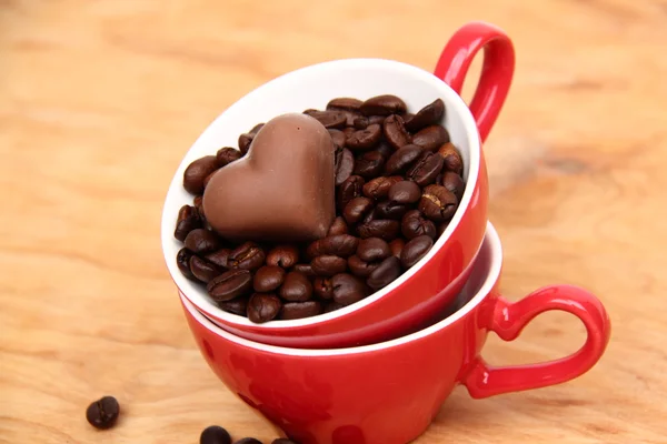 Две чашки с кофейными зёрнами и шоколадными конфетками — стоковое фото
