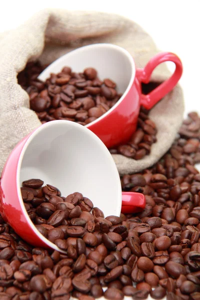 Granos de café en tazas de café rojo de cerámica con símbolo del corazón sobre el saco beige arpillera —  Fotos de Stock
