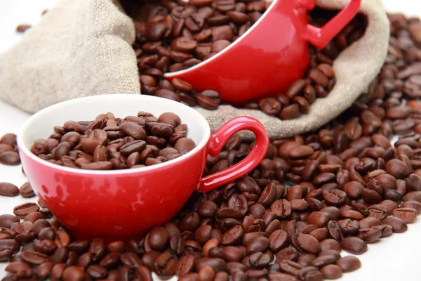 Granos de café en tazas rojas con símbolo del corazón sobre el saco de arpillera —  Fotos de Stock