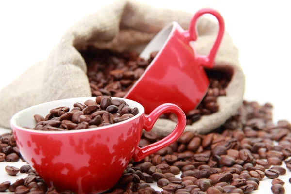 Grãos de café em xícara de café vermelho com símbolo de coração sobre saco de serapilheira — Fotografia de Stock