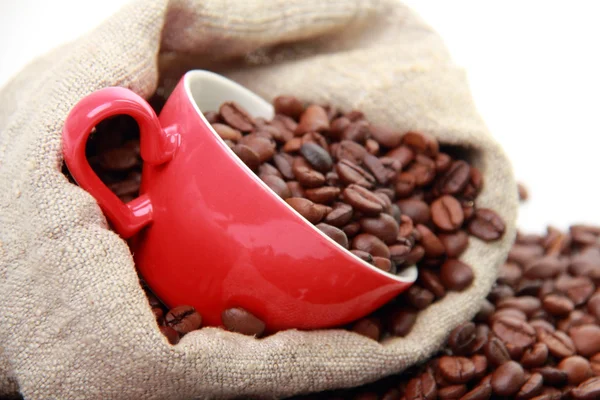 Granos de café en taza roja con símbolo del corazón sobre el saco de arpillera —  Fotos de Stock