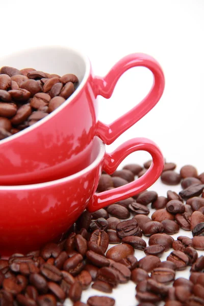 Grãos de café em copo vermelho com símbolo de coração — Fotografia de Stock