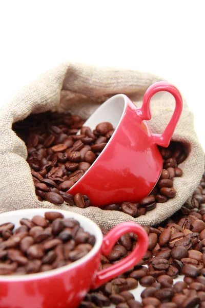 Granos de café en taza roja con símbolo del corazón sobre el saco de arpillera —  Fotos de Stock