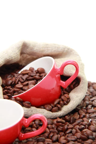 Granos de café en taza roja con símbolo del corazón sobre el saco de arpillera —  Fotos de Stock