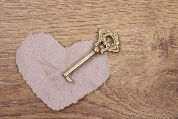 Ancient key with ornament and paper heart on wooden background