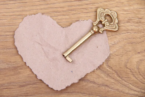 Chiave antica con ornamento e cuore di carta su sfondo di legno — Foto Stock