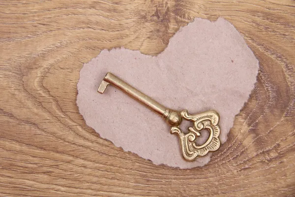 Chiave antica con ornamento e cuore di carta su sfondo di legno — Foto Stock