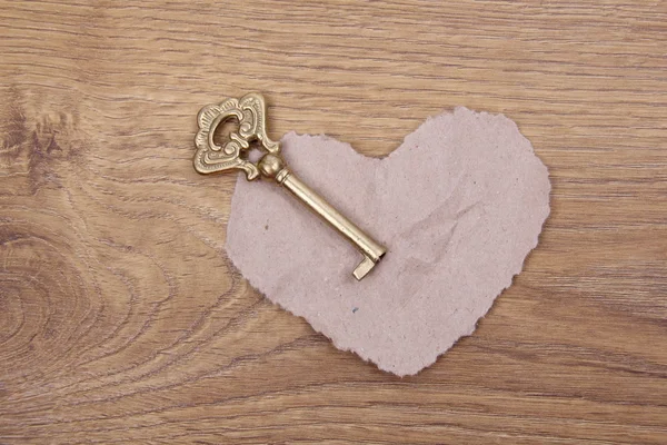 Antique key with ornament and paper heart on wooden background — Stock Photo, Image