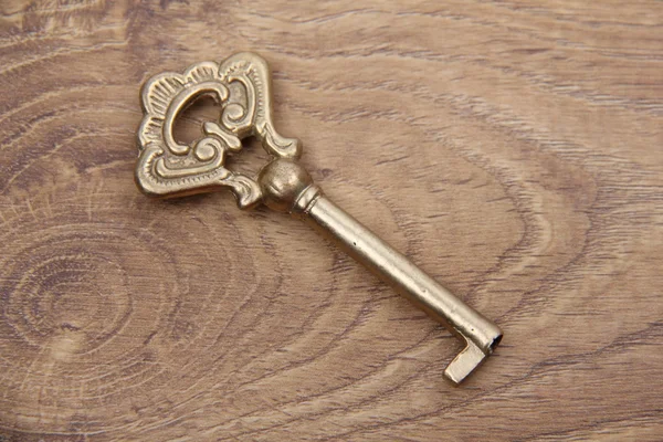 Old metal key with ornament on wooden background — Stock Photo, Image