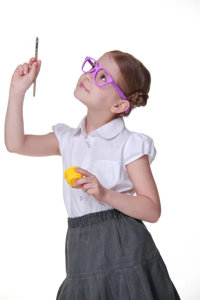 Studio image d'une écolière avec des lunettes posant avec de la peinture et un pinceau — Photo