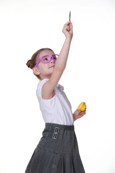 Студийное изображение школьницы с очками, позирующей с краской и кистью — стоковое фото