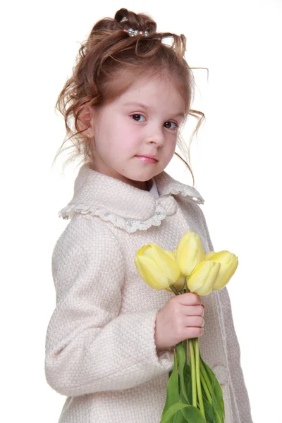 Cute little girl in a coat holding a bouquet of tulips — Zdjęcie stockowe