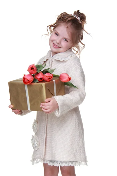 Glad liten flicka i en kappa håller en bukett tulpaner och en presentförpackning — Stockfoto