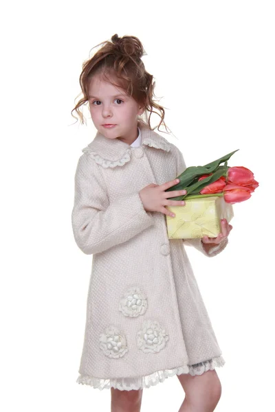 Glückliches kleines Mädchen im Mantel mit einem Strauß Tulpen und einer Geschenkschachtel — Stockfoto