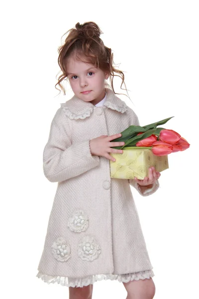 Niña feliz en un abrigo sosteniendo un ramo de tulipanes y una caja de regalo —  Fotos de Stock