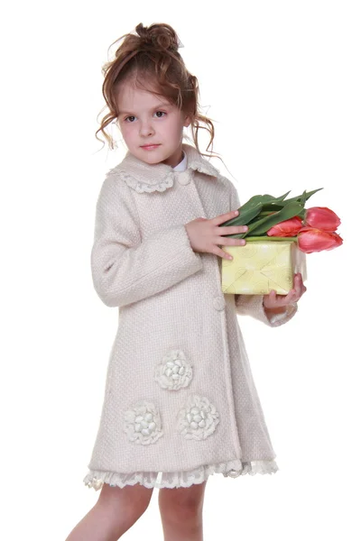 Niña feliz en un abrigo sosteniendo un ramo de tulipanes y una caja de regalo —  Fotos de Stock