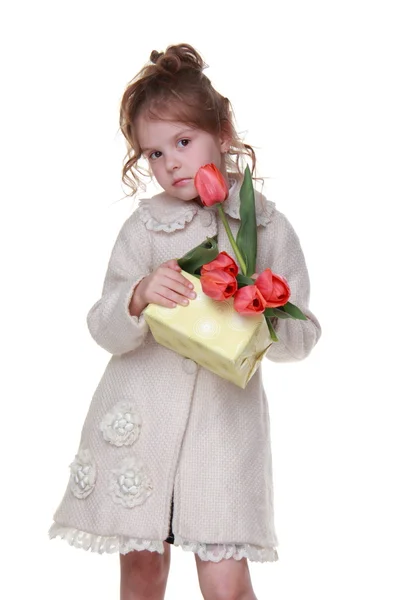 Niña feliz en un abrigo sosteniendo un ramo de tulipanes y una caja de regalo — Foto de Stock