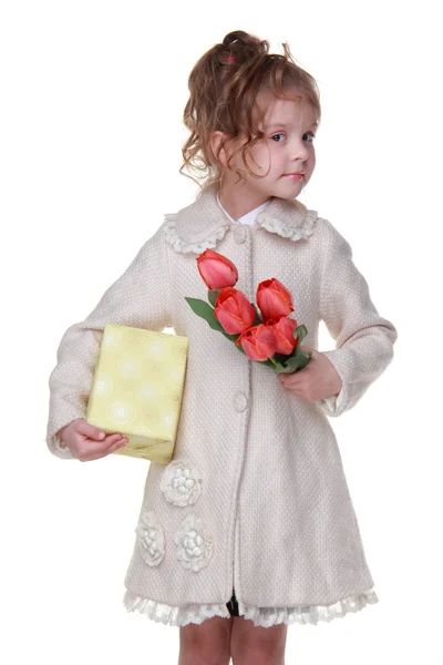 Bonne petite fille dans un manteau tenant un bouquet de tulipes et une boîte cadeau — Photo