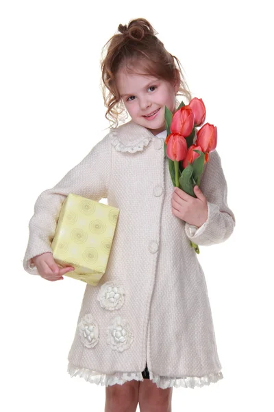 Šťastná holčička v plášti drží kytici tulipánů a dárkový box — Stock fotografie