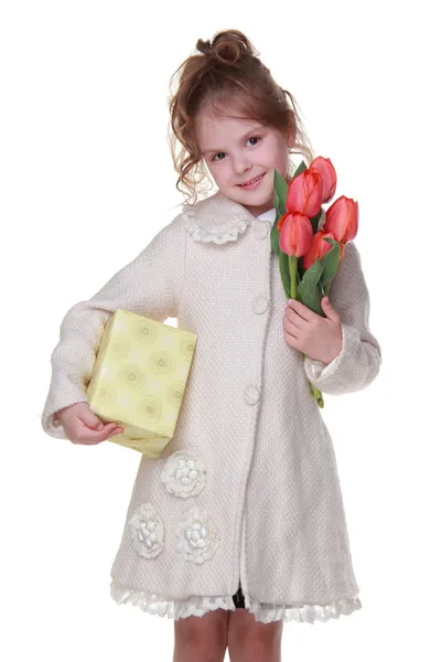 Niña feliz en un abrigo sosteniendo un ramo de tulipanes y una caja de regalo —  Fotos de Stock