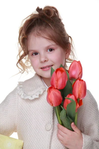 Cute little girl in a coat holding a bouquet of tulips and a gift box — Stock Photo, Image