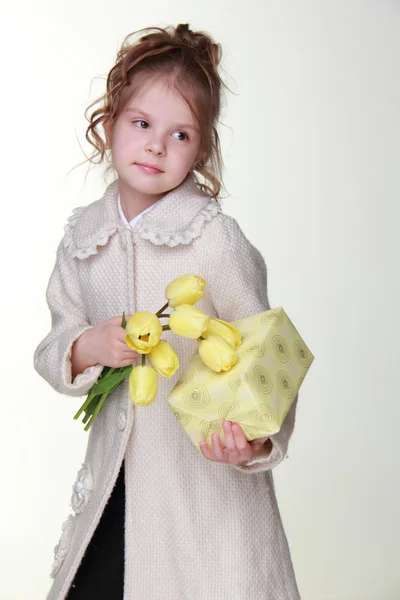 Cute little girl holding a bouquet of tulips and a gift box — Stock Photo, Image