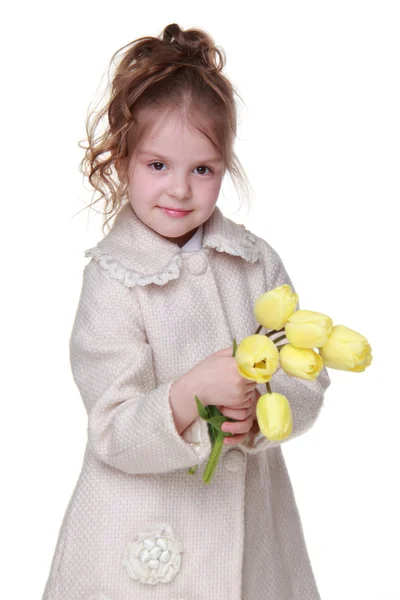 Cute little girl in a coat holding a bouquet of tulips — Zdjęcie stockowe