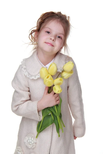 Cute little girl in a coat holding a bouquet of tulips — Zdjęcie stockowe