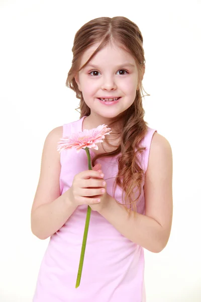 Klein meisje in een lichte jurk bedrijf een gerbera — Stockfoto