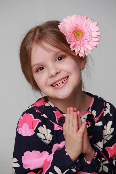 Liten flicka i en klänning med en rosa gerbera i hår — Stockfoto