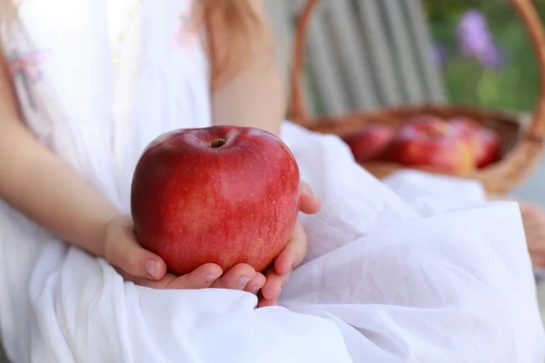 Fille assise sur un banc avec un panier de pommes biologiques rouges avec des pommes rouges sur un banc — Photo