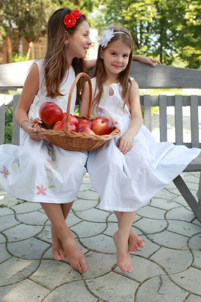 Schöne Mädchen mit einem Korb roter Äpfel auf einer Bank — Stockfoto