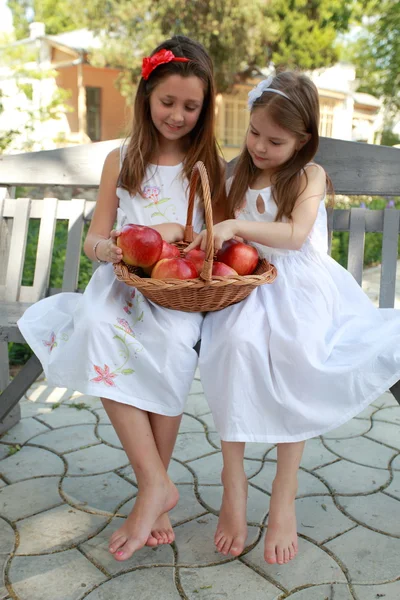 Hermosas chicas con cesta de manzanas rojas en un banco —  Fotos de Stock