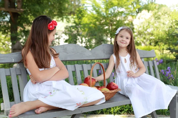 Hermosas chicas con cesta de manzanas rojas en un banco — Foto de Stock