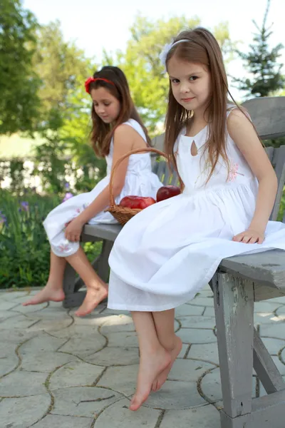 Vackra flickor med korg med röda äpplen på en bänk — Stockfoto