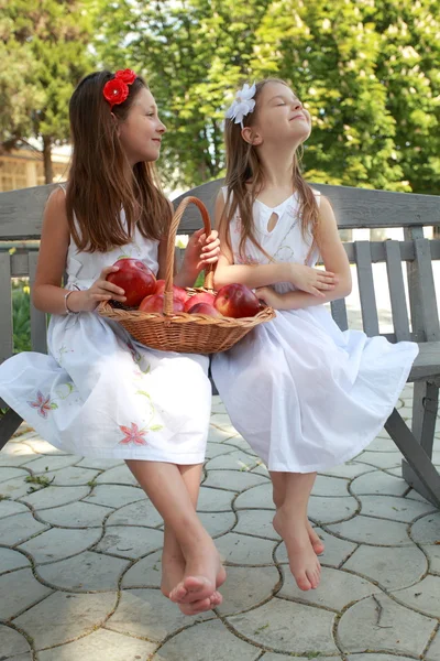 Lovely girls with basket of red apples on a bench — Stok fotoğraf