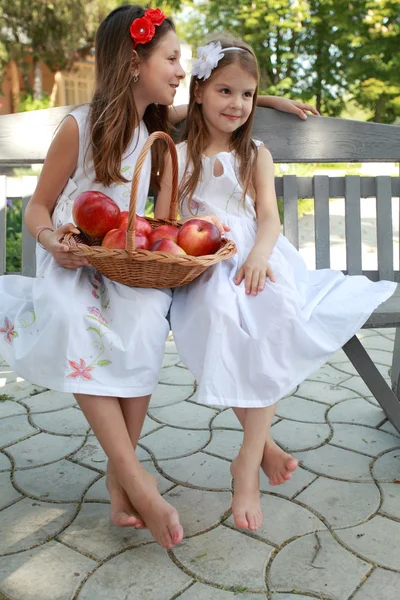 Hermosas chicas con cesta de manzanas rojas en un banco —  Fotos de Stock