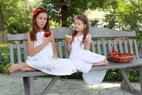 Vackra flickor med korg med röda äpplen på en bänk — Stockfoto
