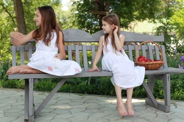 Lovely girls with basket of red apples on a bench — Stockfoto