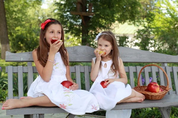 Lovely girls with basket of red apples on a bench — Stok fotoğraf