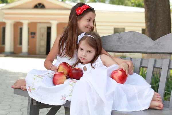 Lovely girls with basket of red apples on a bench — Stok fotoğraf