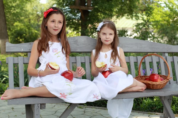 Meninas encantadoras com cesta de maçãs vermelhas em um banco — Fotografia de Stock