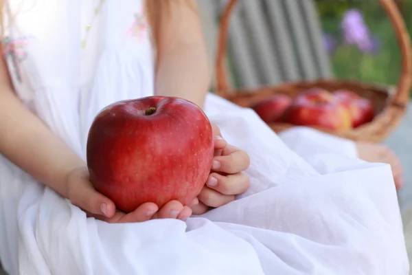 Девушка сидит на скамейке с корзиной из красных органических яблок с красными яблоками на скамейке — стоковое фото