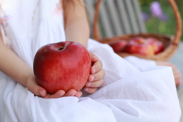 Fille assise sur un banc avec un panier de pommes biologiques rouges avec des pommes rouges sur un banc — Photo