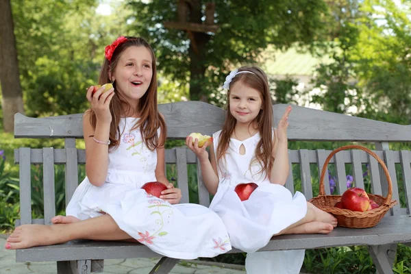 Lovely girls with basket of red apples on a bench — Stockfoto