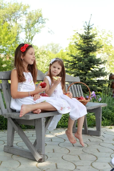 Hermosas chicas con cesta de manzanas rojas en un banco — Foto de Stock