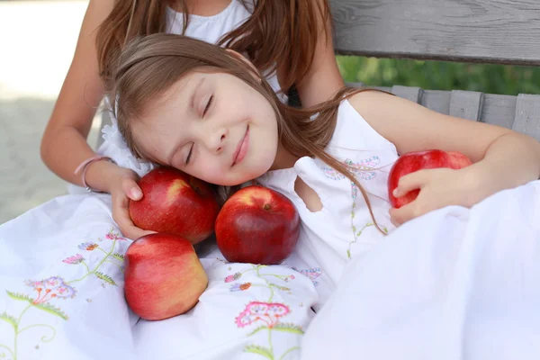 Lovely girls with basket of red apples on a bench — Stockfoto