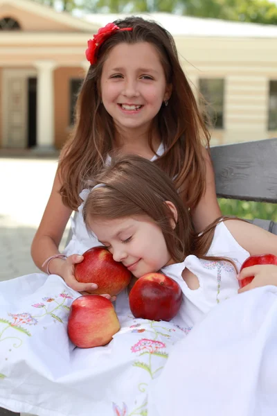 Прекрасные девушки с корзиной красных яблок на скамейке — стоковое фото